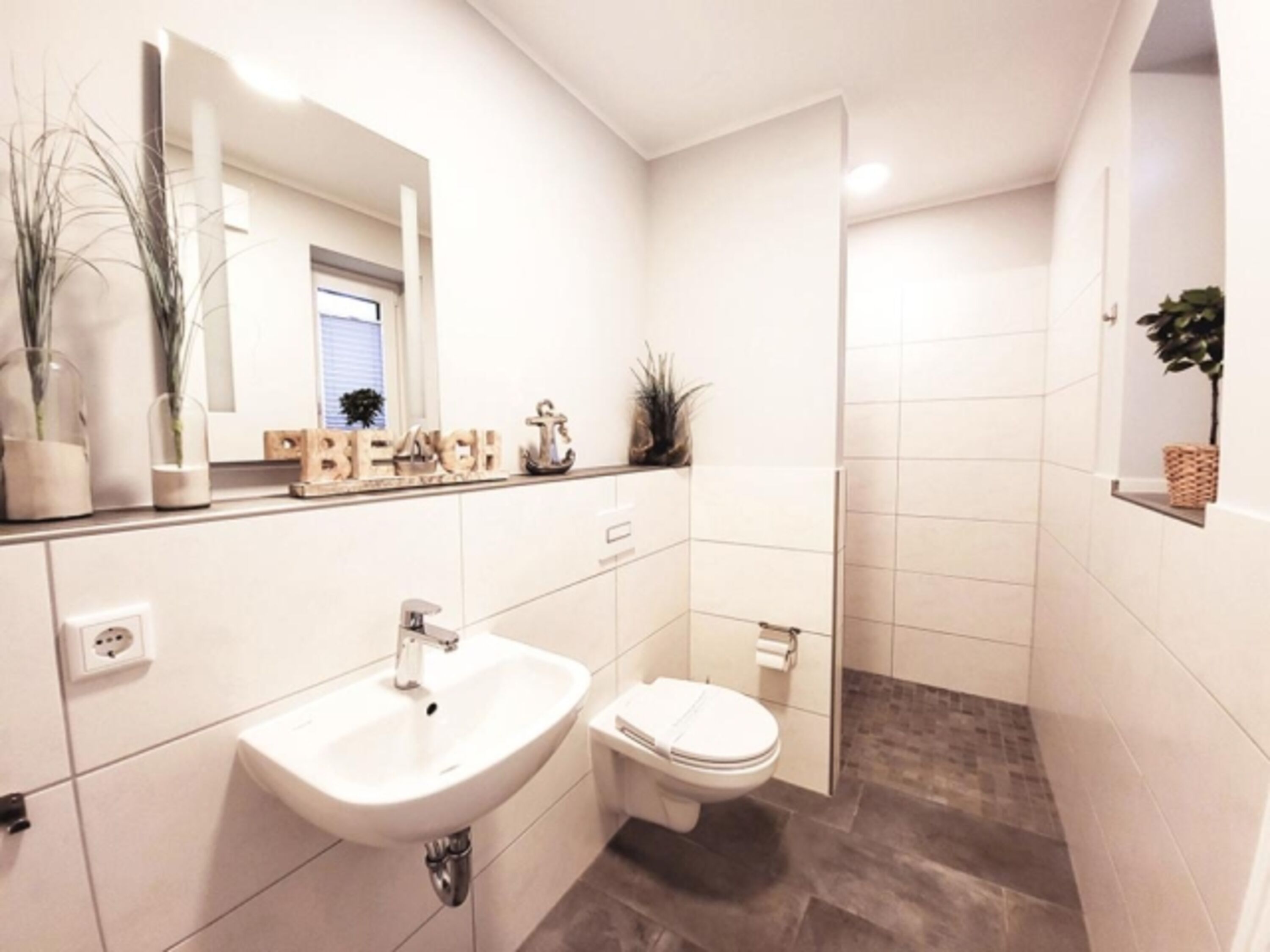 Duschbad mit Erdgeschoss mit bodengleichem Duschbereich, WC, Waschbecken und zwei Fenster
