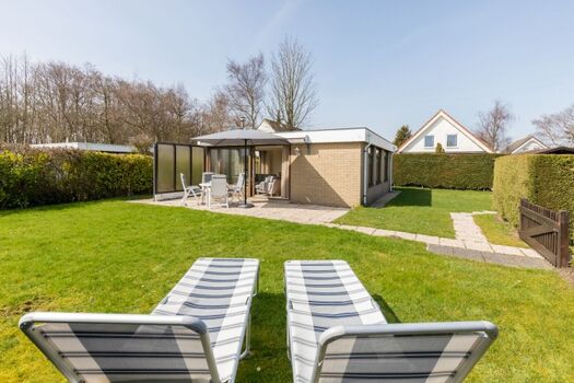 Der große, eingezäunte Garten mit Liegen, Sonnenschirm, Grill