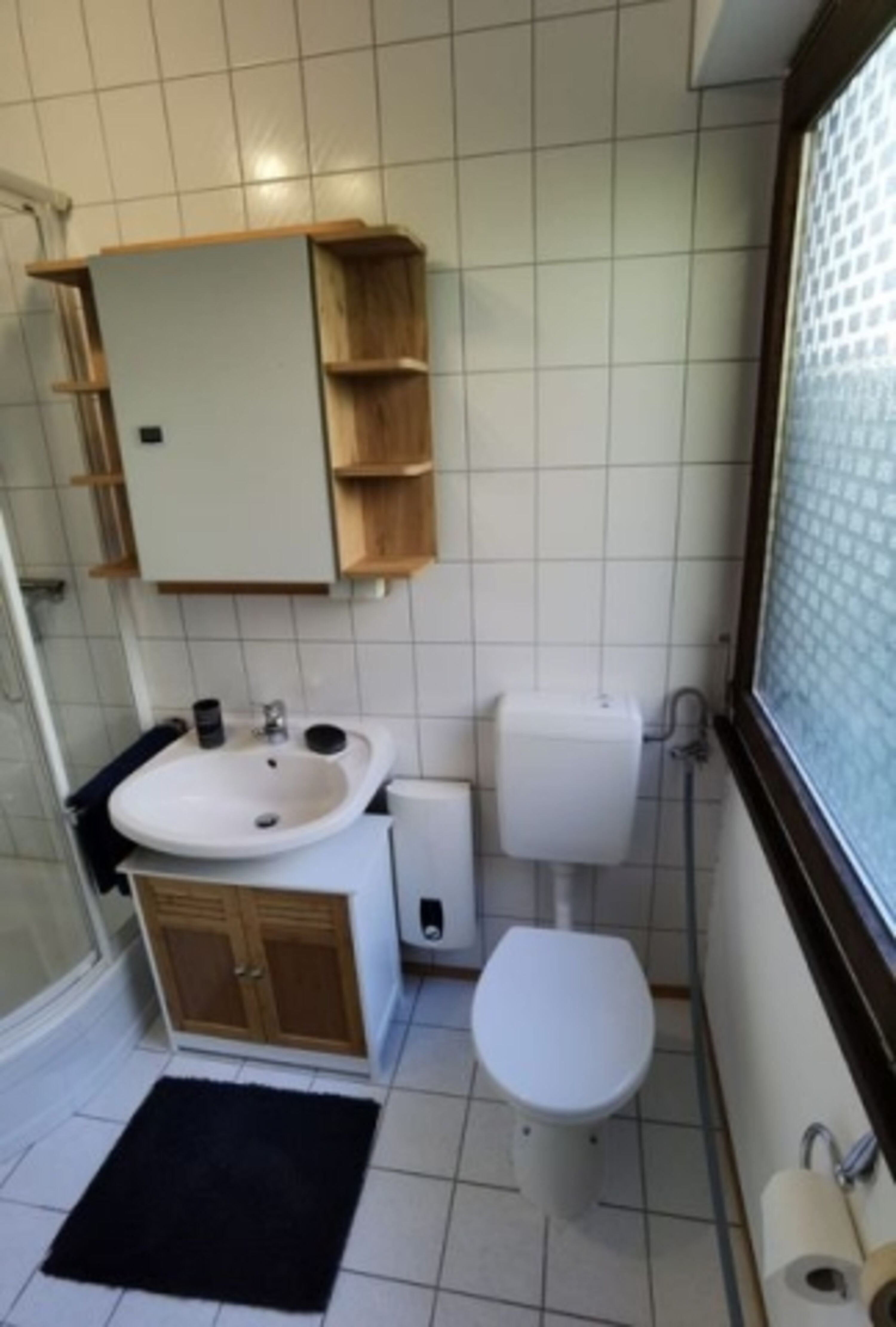 Unser Badezimmer verfügt über eine großzügige Dusche, ein Waschbecken mit Spiegelschrank und Unterschrank, eine Toilette, eine Waschmaschine und eine Infrarotheizung.