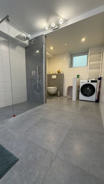Bad 1 mit Barrierefreier großer Dusche, Doppel Waschbecken, Toilette und Waschmaschine.
