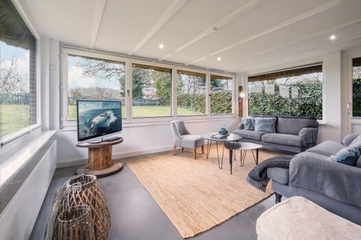 Heller Wintergarten als Wohnzimmer mit TV und Gartenblick