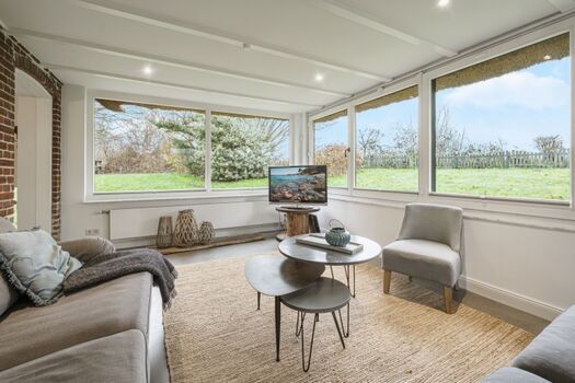 Heller Wintergarten als Wohnzimmer mit TV und Gartenblick