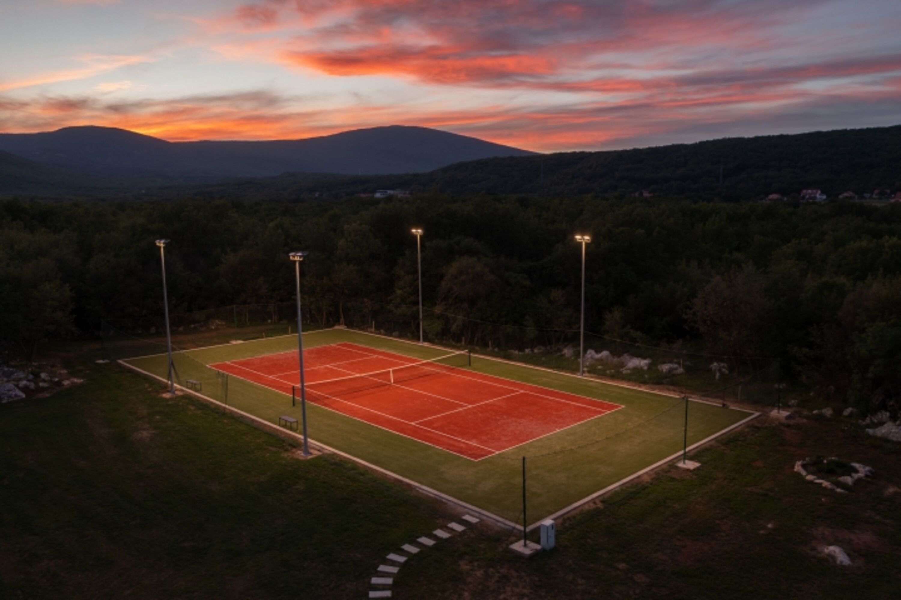 Ein Tennisplatz im Freien mit Kunstrasen und Tennisausrüstung und mit Beleuchtung für Abendspiele