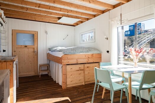 Der Hauptraum mit Küchenzeile, Bett und Esstisch; durch die Tür kommt man ins Bad, dort ist auch der Eingang