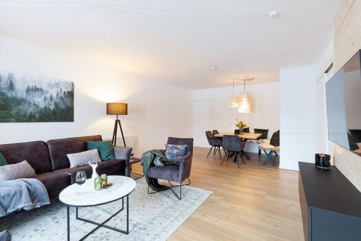 Wohnraum mit Sofa, Sesseln und Essbereich und Smart TV