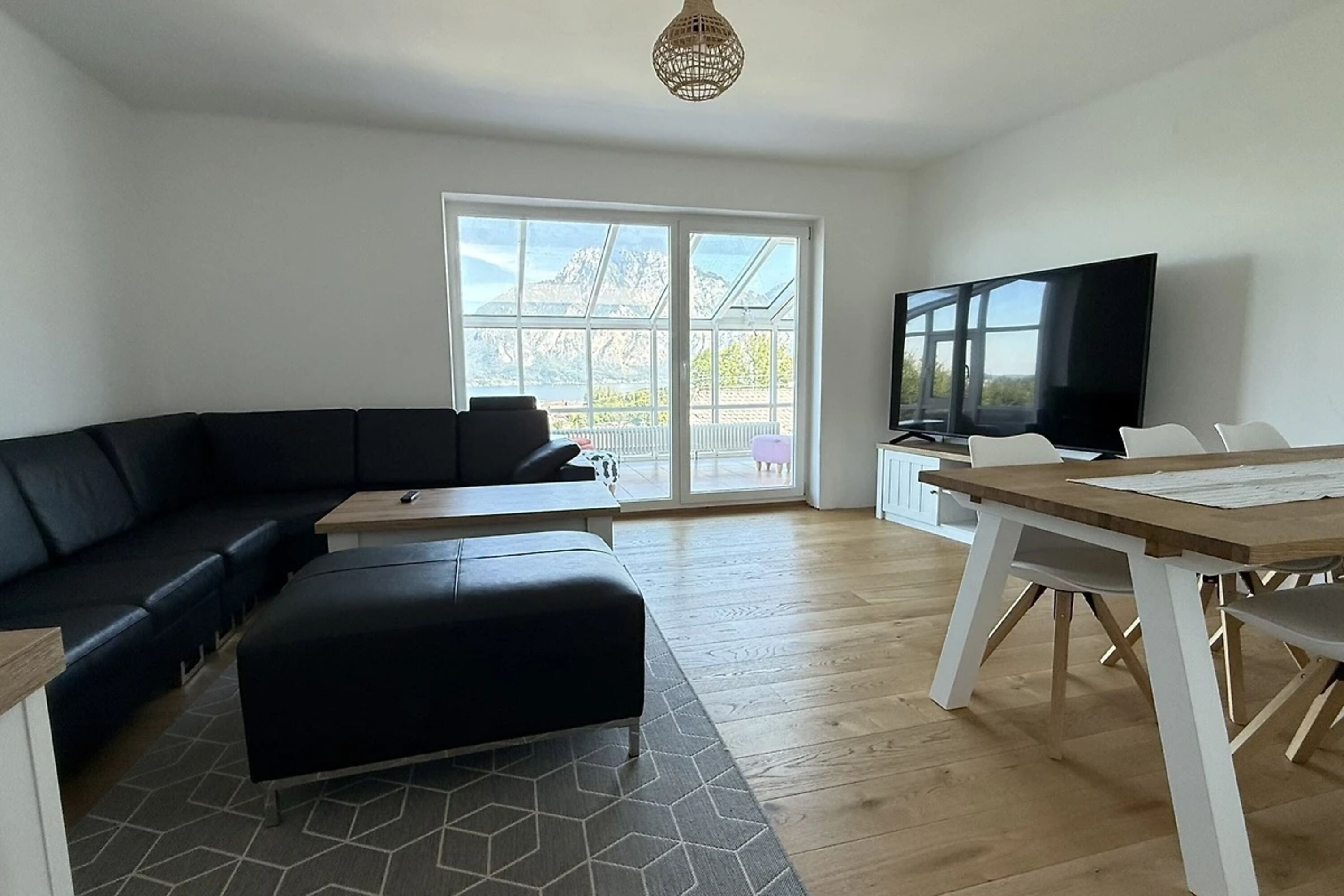 Wohnzimmer mit verglastem Wintergarten, Ledercouch, großem Esstisch und 85 Zoll Flat TV.