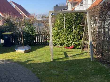 Schaukel und Sandkasten im eingezäunten Garten
