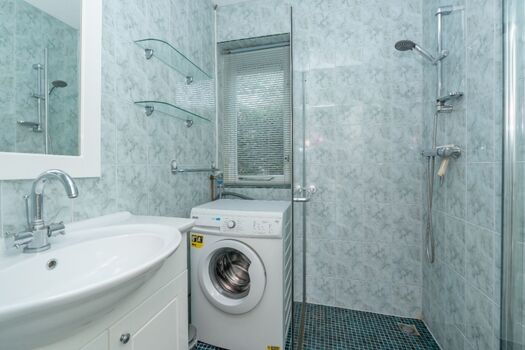 Das Badezimmer mit Dusche, Waschbecken und Waschmaschine