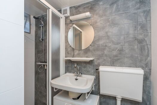 Der Badezimmer mit Dusche, Waschbecken und WC