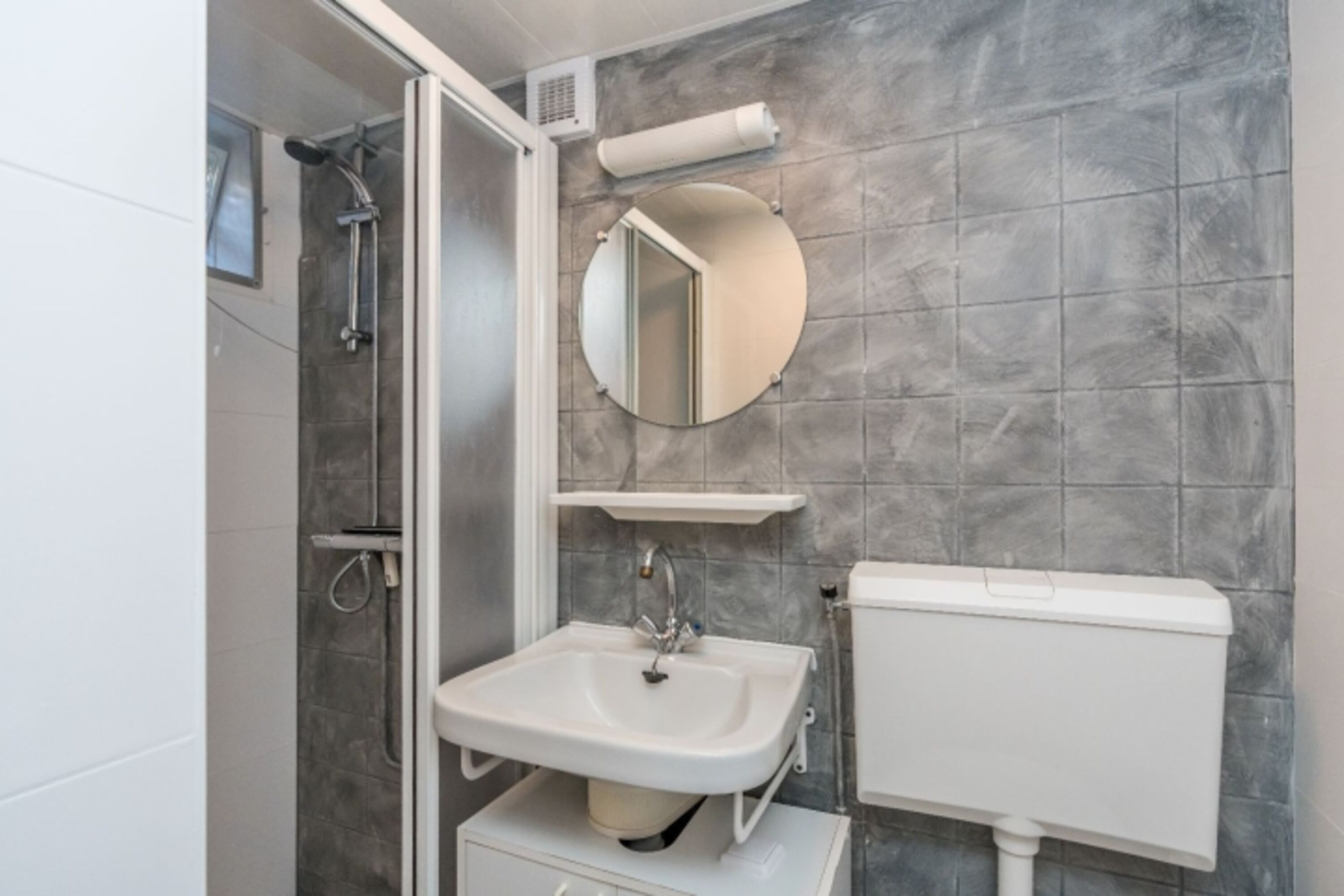 Der Badezimmer mit Dusche, Waschbecken und WC