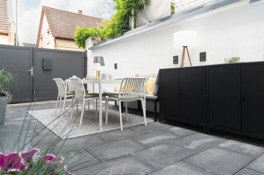 Terrasse (21 m²) im Hof: Außenküche mit elektrischem Grill und Spüle, viel Stauraum, Esstisch, Stühle und gepolsterte Sitzbank für 8 Personen, echte Topfpflanzen und Außenbeleuchtung – perfekt für gemeinsames Frühstück und entspannte Grillabende