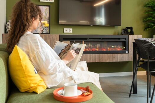 Gemütliches Wohnzimmer mit bequemer Couch, 55'' Smart-TV über modernem Elektrokamin und ausziehbarem Esstisch mit Bank 