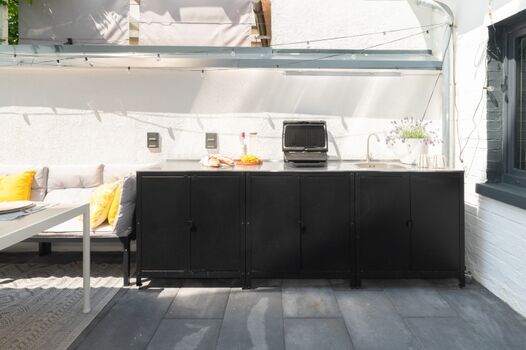 Terrasse (21 m²) im Hof: Außenküche mit elektrischem Grill und Spüle, viel Stauraum, Esstisch, Stühle und gepolsterte Sitzbank für 8 Personen, echte Topfpflanzen und Außenbeleuchtung – perfekt für gemeinsames Frühstück und entspannte Grillabende