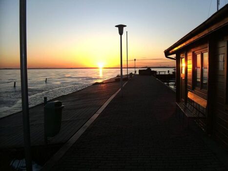 Sonnenuntergang bei zugefrorenem See am Bootsanleger der Segelschule Schlick
