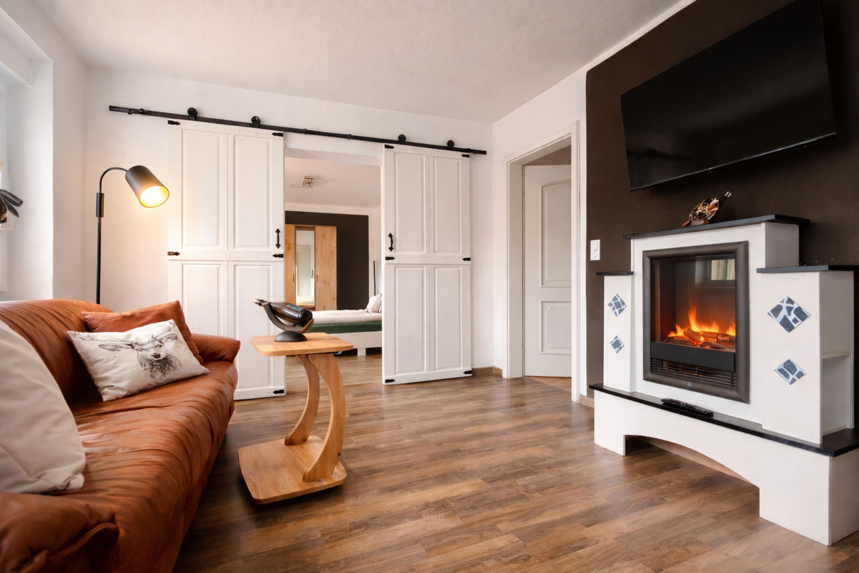Kleines Wohnzimmer mit TV und Elektrokamin mit Blick ins große Schlafzimmer