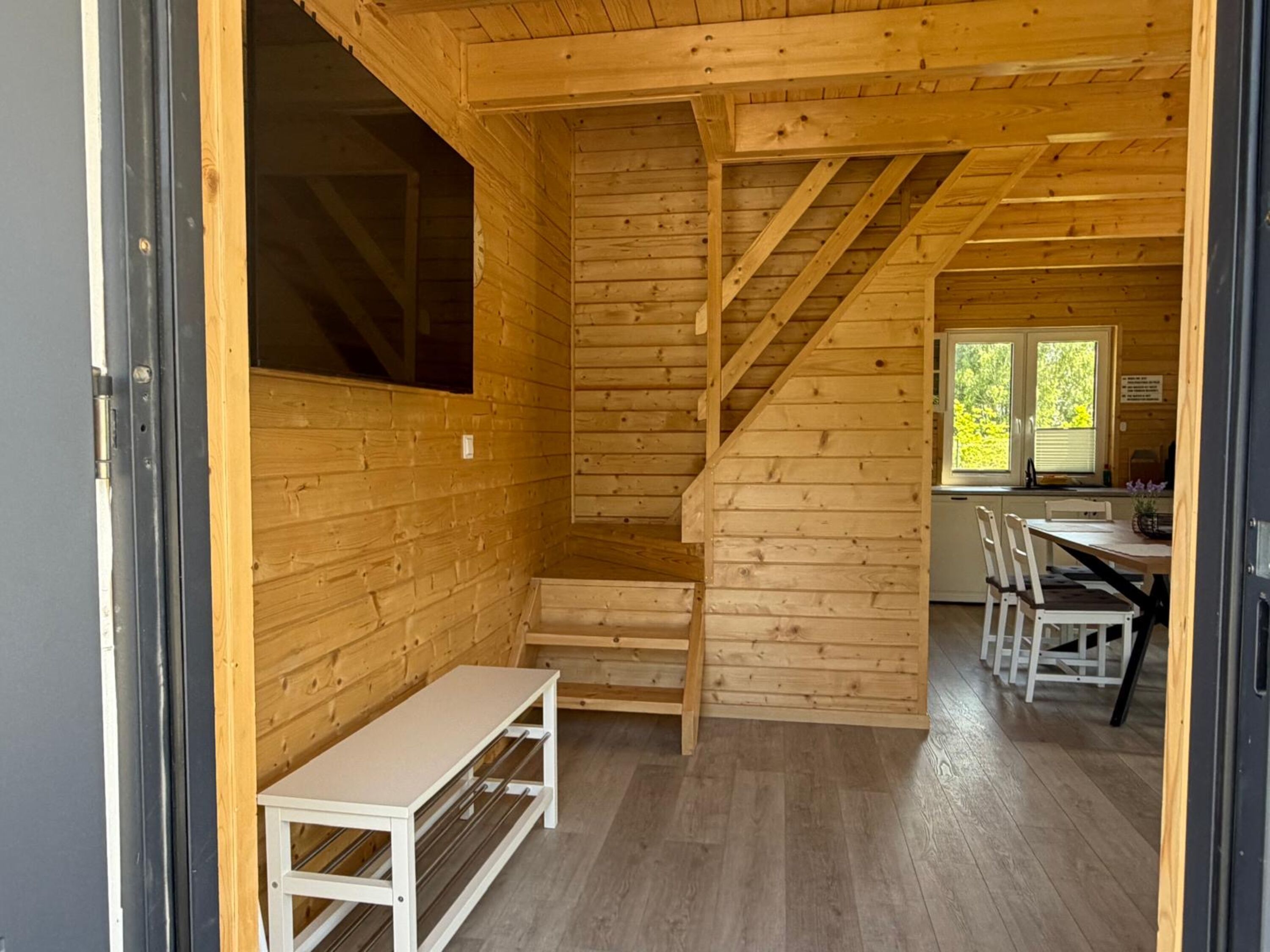 Heller Eingangsbereich mit Holzverkleidung, TV, Garderobe und Blick auf den Essbereich.