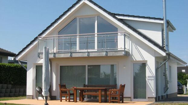 Süd-Ost-Seite mit der Fensterfront vom Wohnzimmer. Davor die Terrasse mit dem Grill und der grosse eingezäunte Garten. Oben befindet sich die Galerie, bzw. das zweite Wohnzimmer mit klasse Meerblick, weiterem TV, gemütlicher Couch und hochwertigem 180er S